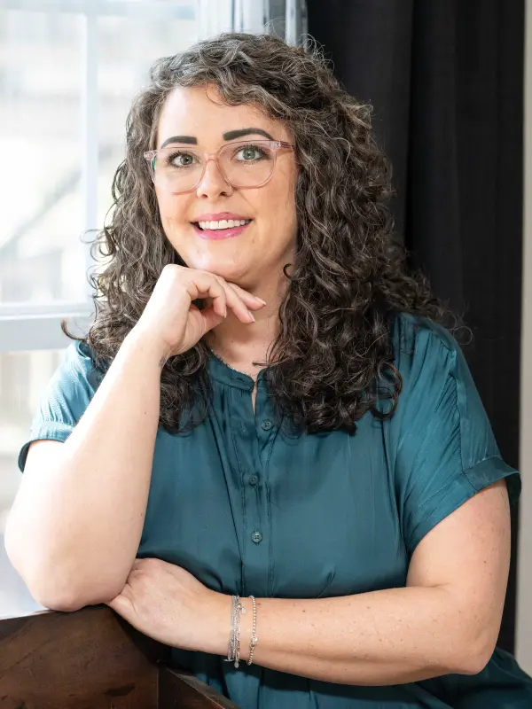 A woman with curly hair and glasses posing for the camera.