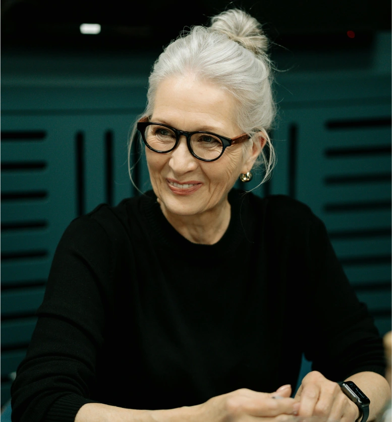 A woman with white hair and glasses sitting at a table.